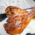 Two BBQ slow cooker drumsticks on top of some mashed potatoes.