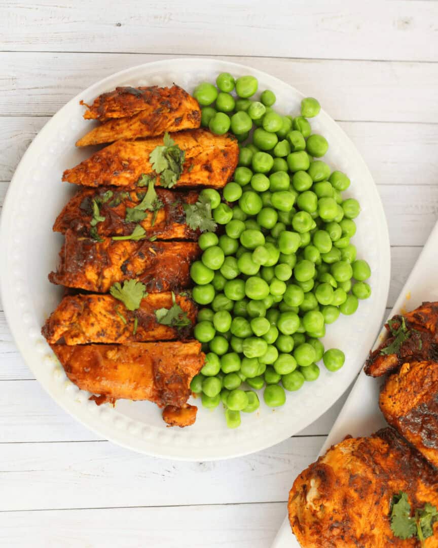 Garlic Butter chicken tenders with a side of peas on a white plate.