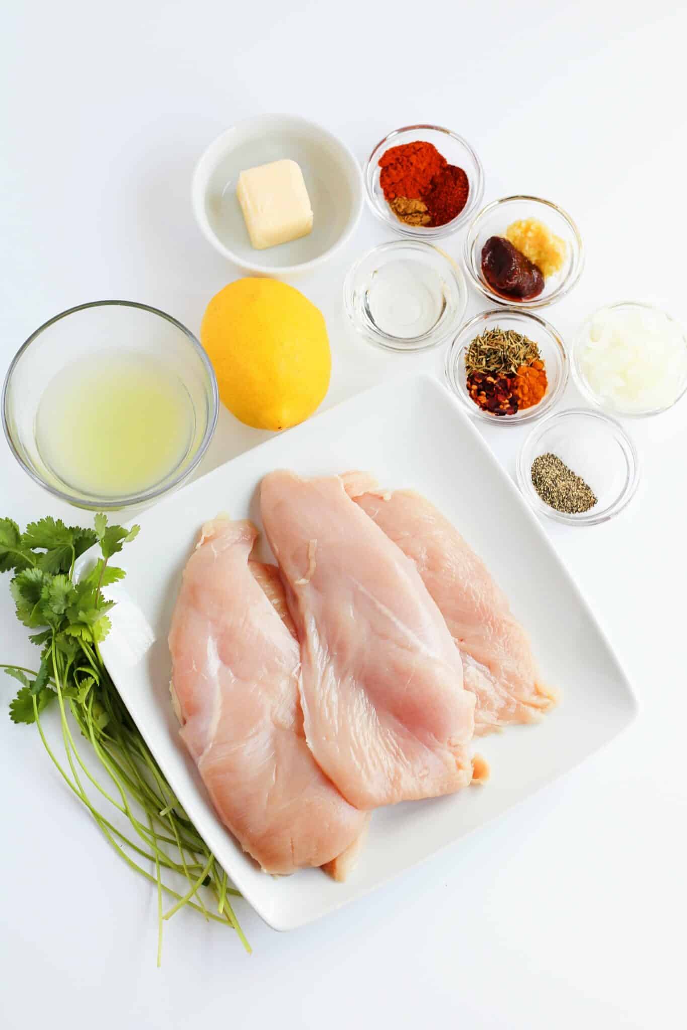 Ingedients for Garlic butter chicken tenderloins including chicken breasts, lemon, seasonings and butter.