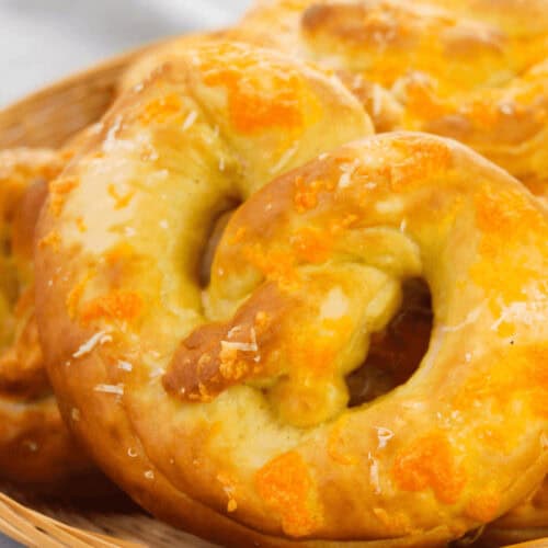 A wicker basket brimming with Philly soft pretzels, each generously topped with melted cheese, rests invitingly on a light fabric background.