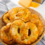 A basket of cheese-topped snack rests on a gray cloth, with a grater and block of cheese in the background.