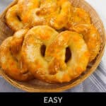 A basket of freshly baked Philly soft pretzels topped with melty cheese rests on a striped cloth, while a tempting block of cheese sits in the backdrop.