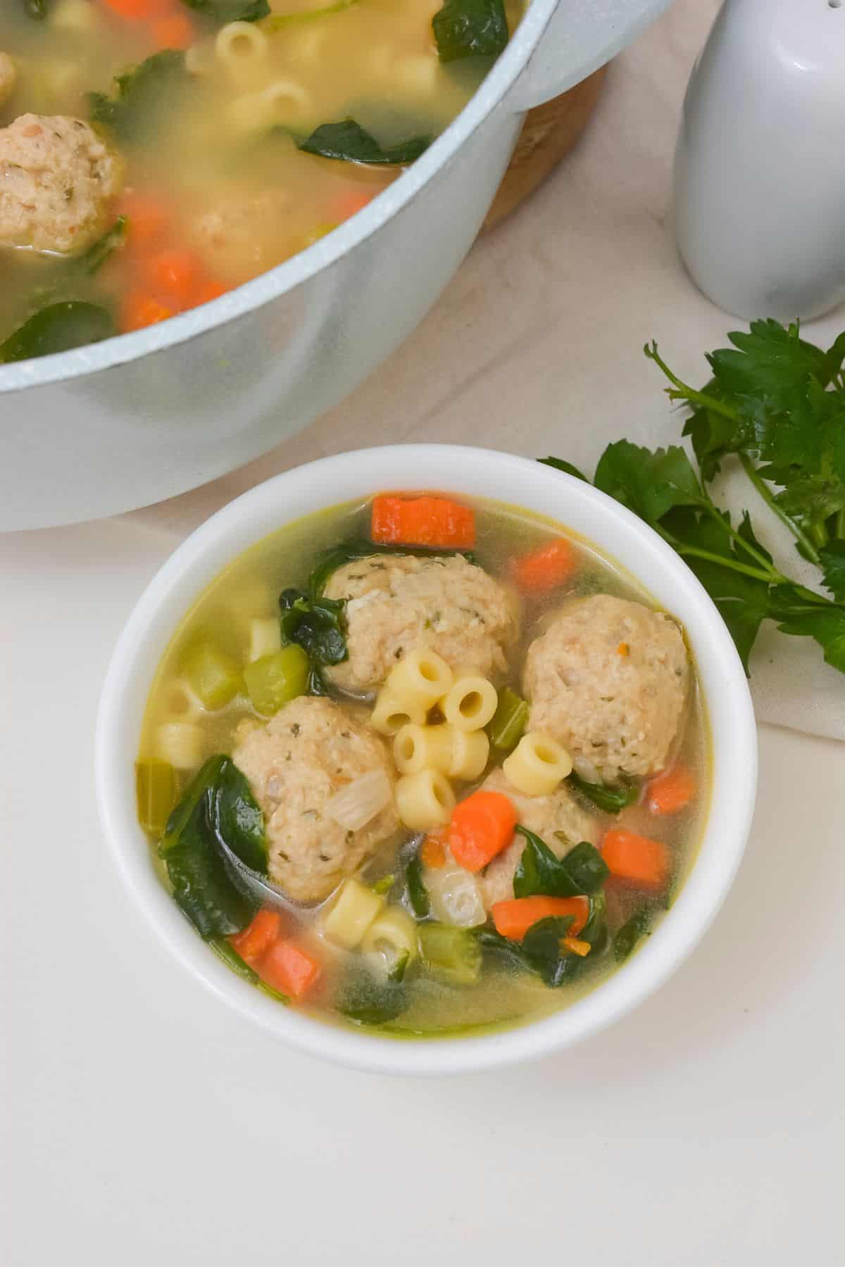 A bowl of the italian wedding soup recipe beside the pot.