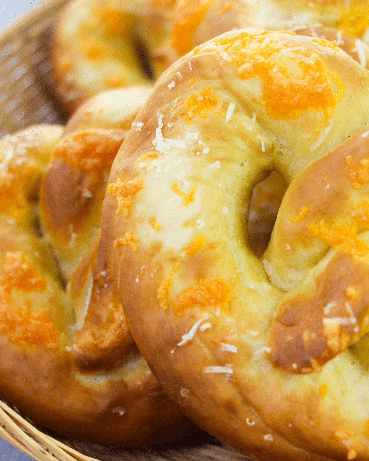A close up of soft pretzels with cheese stacked on a woodlen plate.