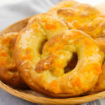 Soft pretzels with cheese stacked on a woodlen plate.