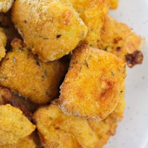 Close-up of golden-brown, breaded tofu nuggets stacked on a white plate, resembling the crispy texture of Air Fryer Catfish Nuggets.
