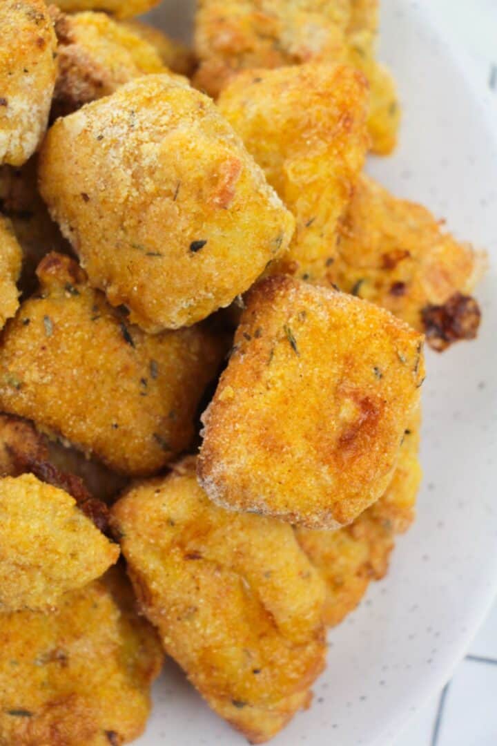 Close-up of golden-brown, breaded tofu nuggets stacked on a white plate, resembling the crispy texture of Air Fryer Catfish Nuggets.