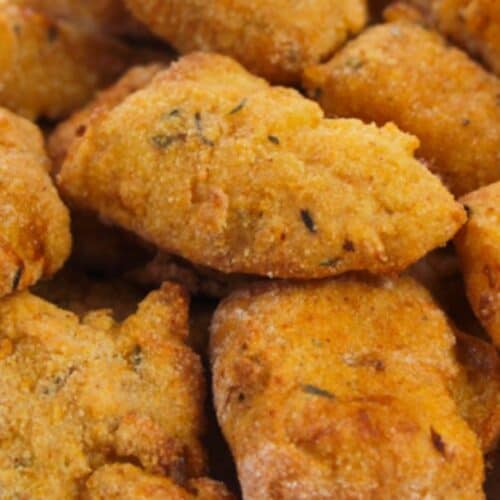 Close-up of several pieces of golden-brown, seasoned fried okra on a white surface, perfectly paired with crispy Air Fryer Catfish Nuggets for a delicious Southern-inspired meal.