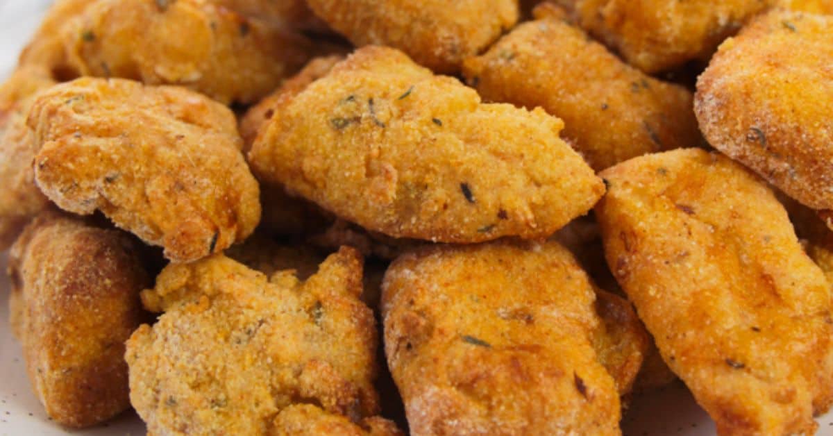 Close-up of several pieces of golden-brown, seasoned fried okra on a white surface, perfectly paired with crispy Air Fryer Catfish Nuggets for a delicious Southern-inspired meal.