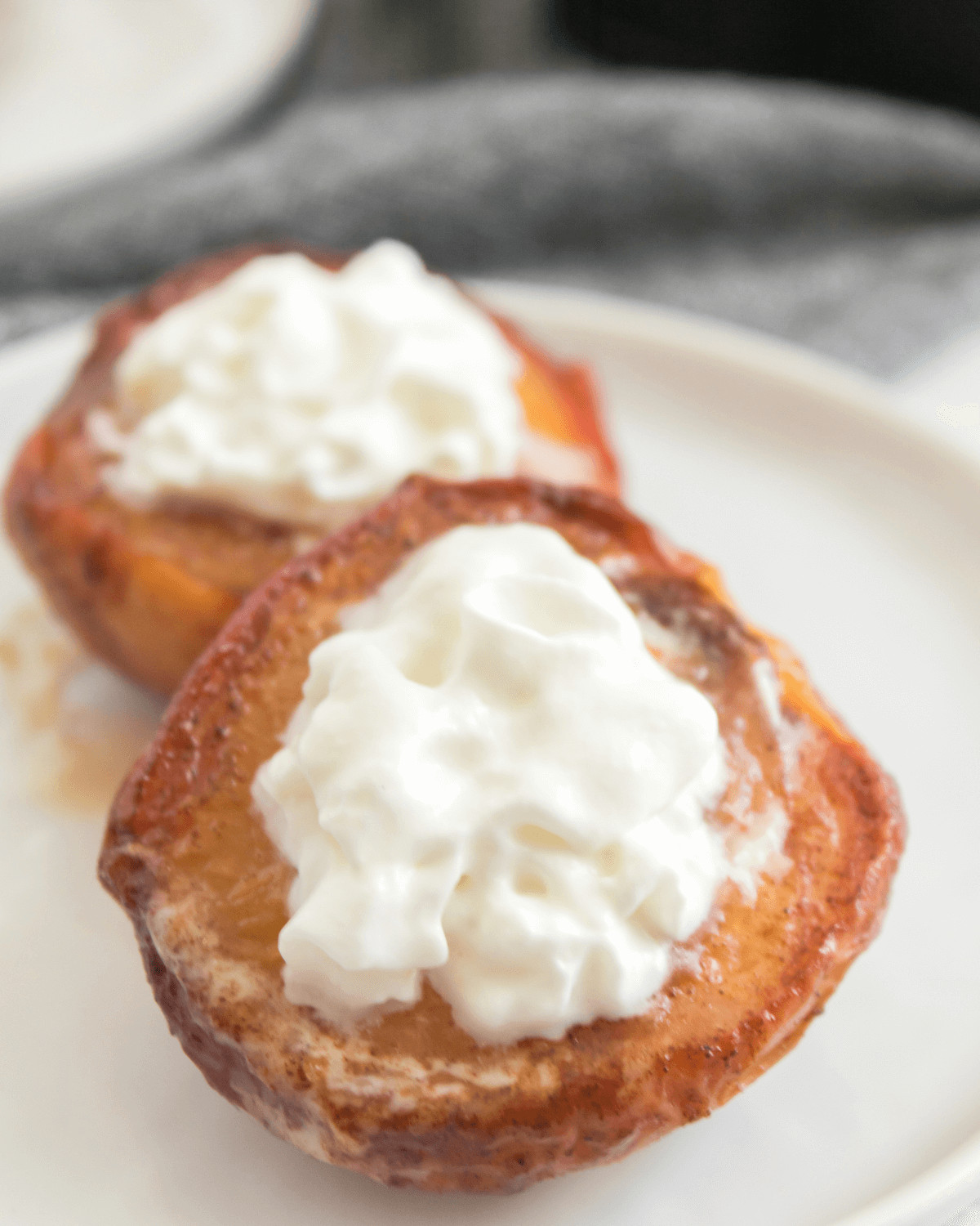 Air fryer peaches on a white plate with whipped cream.