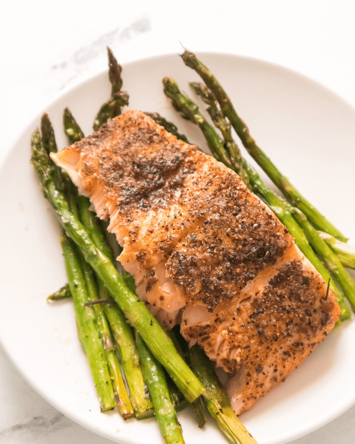 A white plate with asparagus and a seasoned salmon piece.