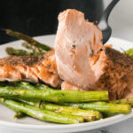 A piece of the salmon on a fork with asparagus on the plate.