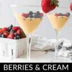 Two martini glasses filled with a creamy dessert topped with blueberries and raspberries, each garnished with a strawberry. In the background is a white container with more berries. Text reads "Berries and Cream Copycat Ruth Chris Recipe.