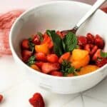 A raspberry next to the bowl of the finished fruit.
