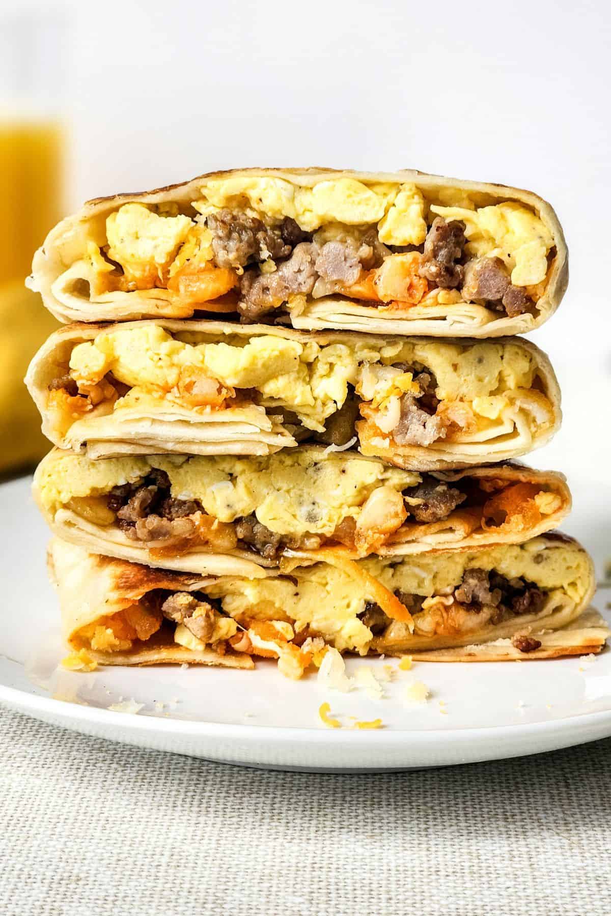 Four breakfast burritos cut in half, stacked on a white plate, filled with scrambled eggs, sausage, cheese, and potatoes—each bite delivering the hearty flavors of a classic Breakfast Crunchwrap.