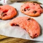 Three treats on parchment paper, one with a bite taken out, rest on a wooden board with a cloth in the background.