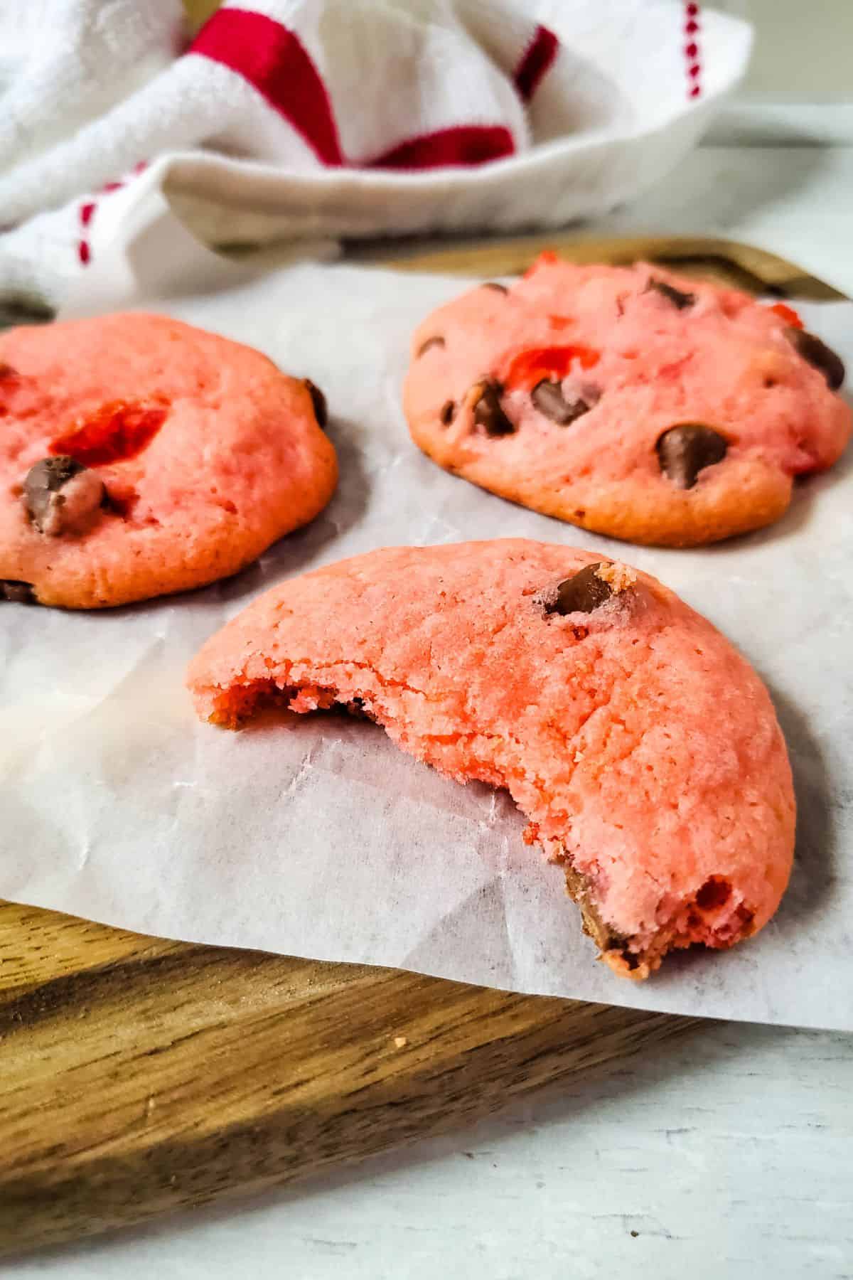 Three treats on parchment paper, one with a bite taken out, rest on a wooden board with a cloth in the background.