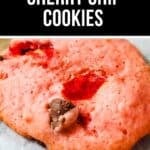 A close-up of a soft, pink Cherry Chip Cookie with visible chocolate chips and cherry pieces on parchment paper.