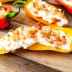 Stuffed Mini Peppers are halved and filled with a creamy mixture, then topped with bacon bits and beautifully arranged on a wooden serving board.