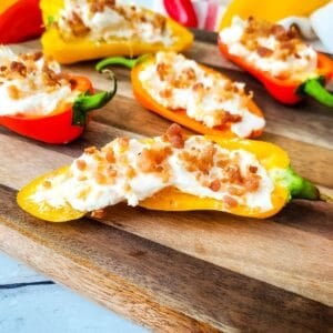Stuffed Mini Peppers halved and filled with a creamy cheese mixture, topped with crumbled bacon, arranged on a wooden serving board for an irresistible appetizer.