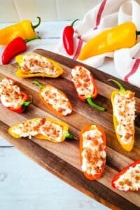Stuffed Mini Peppers halved and filled with a creamy cheese mixture, topped with crispy bacon bits, are beautifully arranged on a wooden serving board.