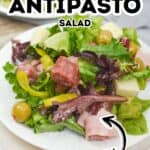 A plate of Antipasto Misto salad with mixed greens, salami, cheese cubes, green olives, and yellow peppers, labeled "FRESH.