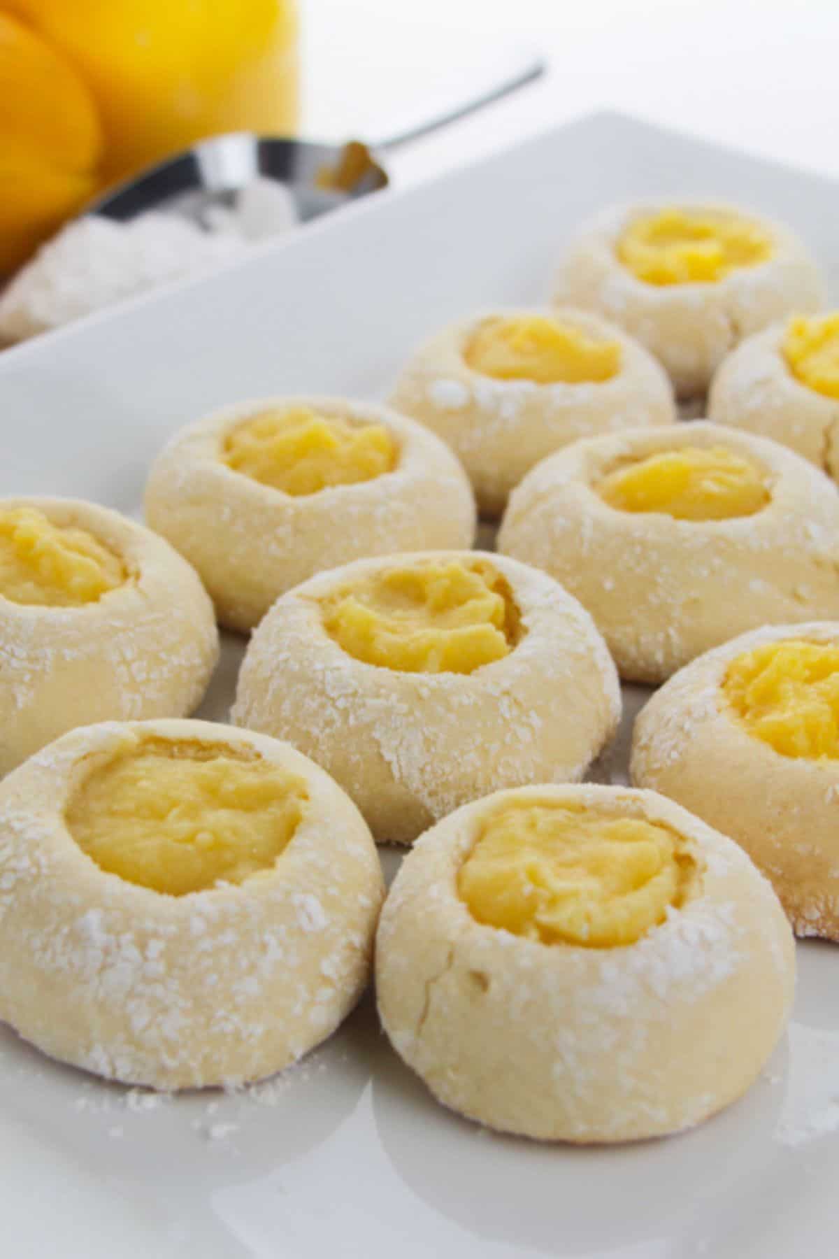 Round Lemon Curd Cookies with powdered surfaces and indented centers filled with bright yellow custard, arranged on a white plate.