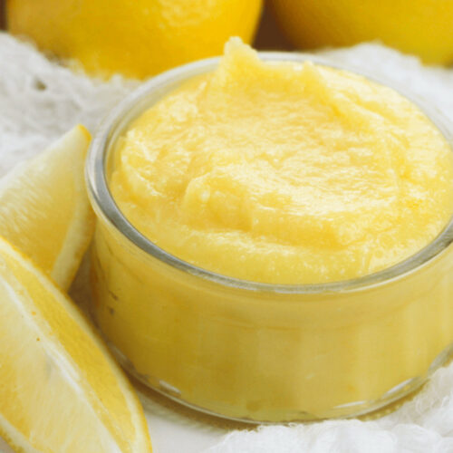 A glass dish of the lemon curd with lemons on the side.
