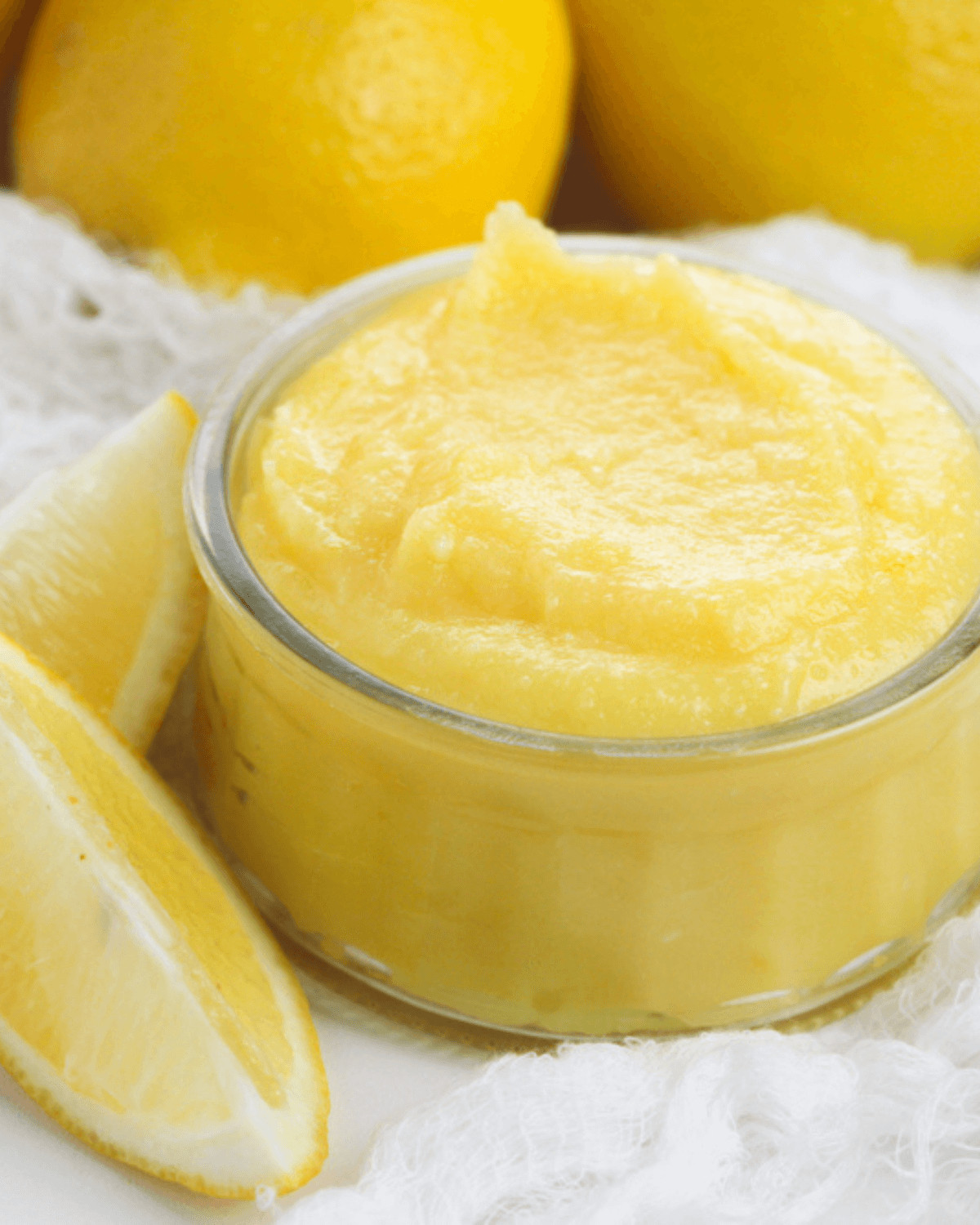 A glass dish of the lemon curd with lemons on the side.