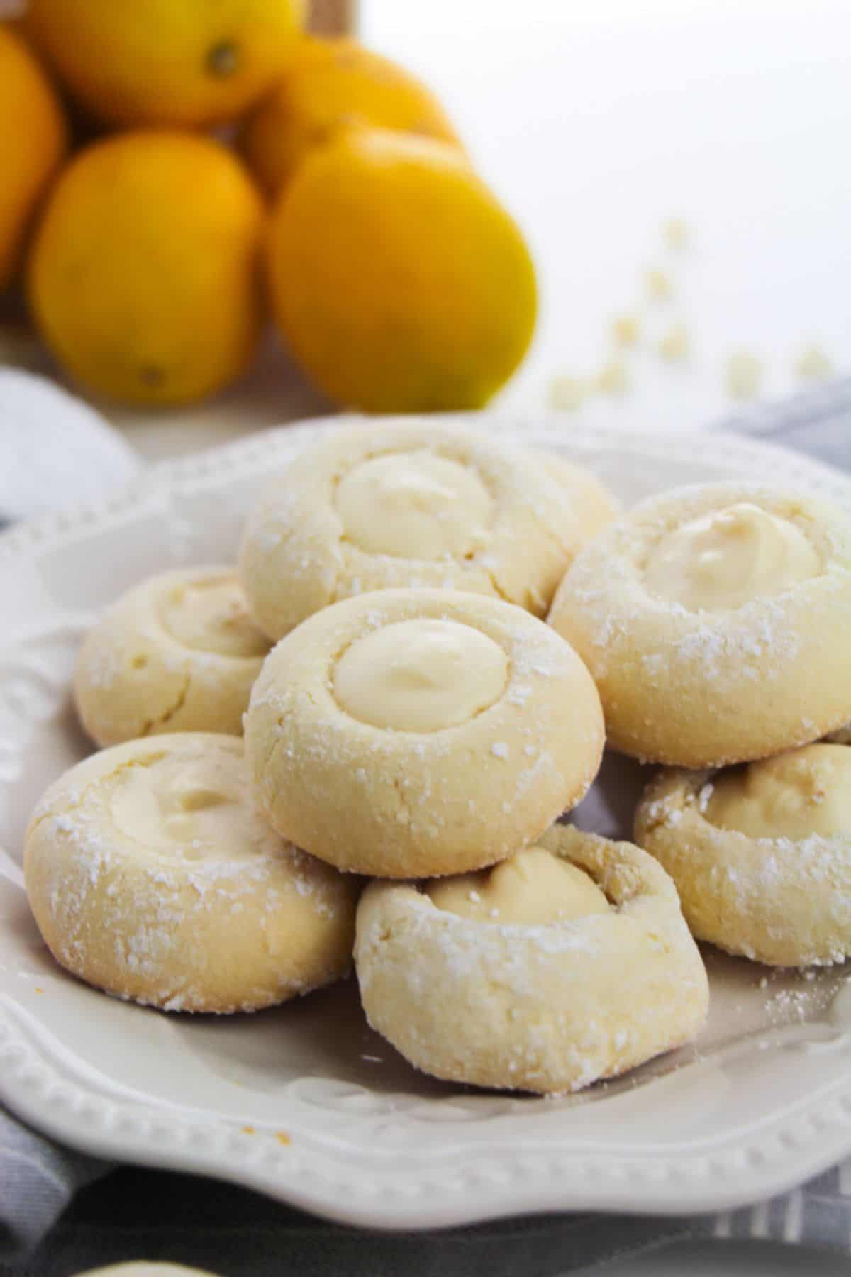 A white plate holds several dusted with powdered sugar, each filled with a creamy center. Whole lemons are visible in the background.