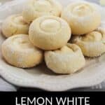 A plate of Lemon White Chocolate Cookies, each with a creamy white chocolate center, is displayed with fresh lemons in the background.