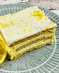A slice of Lemon Icebox Cake on a green plate, garnished with lemon zest and a lemon slice. The cake has visible layers of crackers and lemon filling.