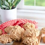 No Bake Peanut Butter Oatmeal Cookies are arranged on a wooden board and marble slab, with a red polka dot cloth and a potted plant in the background by a window.