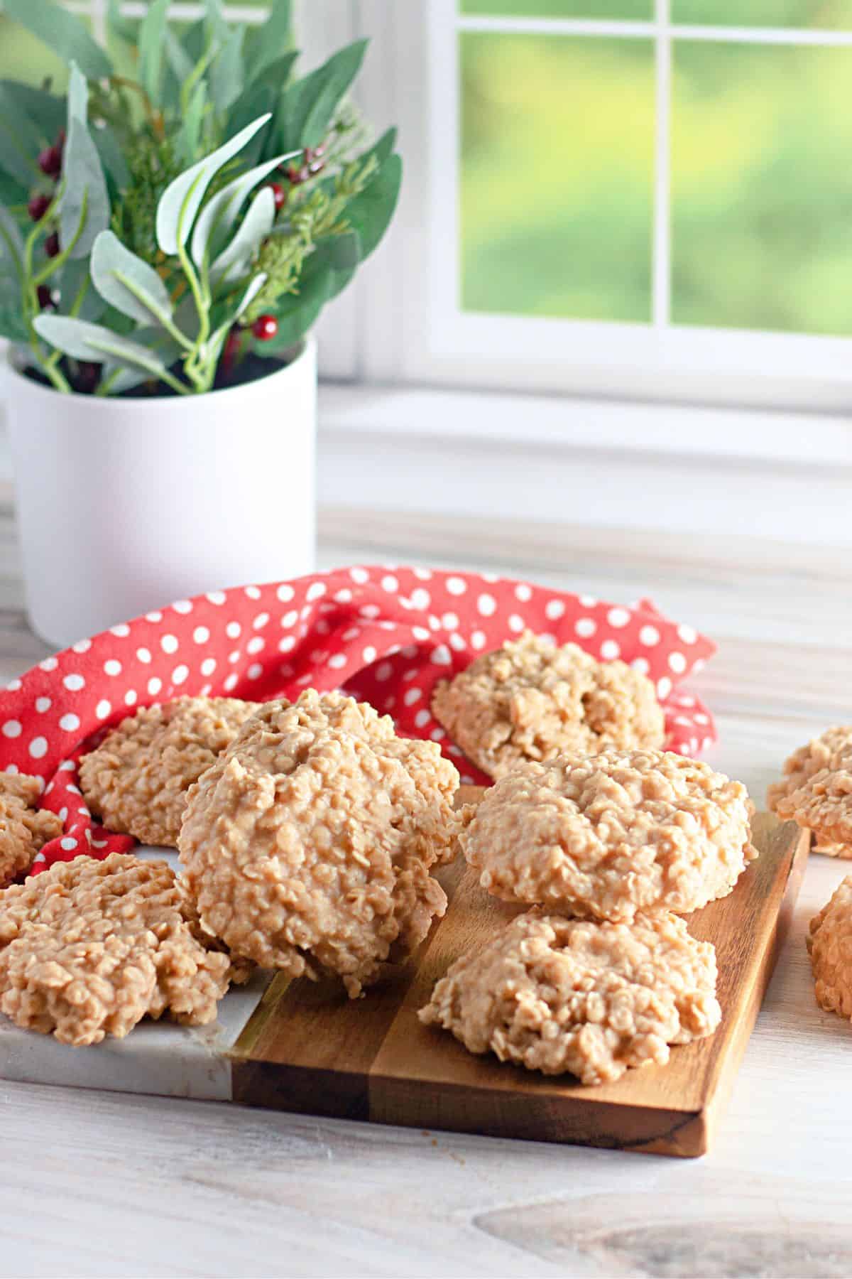 No Bake Peanut Butter Oatmeal Cookies are arranged on a wooden board and marble slab, with a red polka dot cloth and a potted plant in the background by a window.