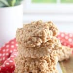 A stack of No Bake Peanut Butter Oatmeal Cookies sits on a marble surface with a red and white polka dot cloth and a potted plant in the background.