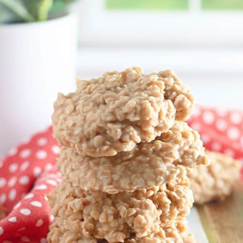A stack of No Bake Peanut Butter Oatmeal Cookies sits on a marble surface with a red and white polka dot cloth and a potted plant in the background.