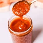 A spoonful of thick, reddish-orange sauce in a jar.
