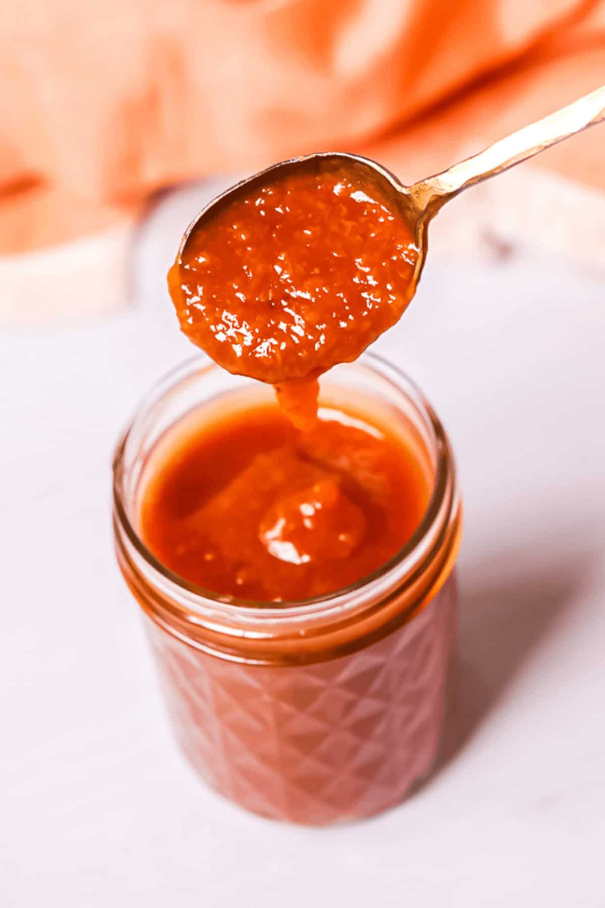 A spoonful of thick, reddish-orange sauce in a jar.