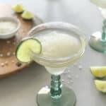 A glass full of the drink with slices of lime around it.