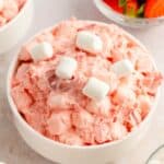 A delightful bowl of pink fruit salad, topped with fluffy marshmallows, takes center stage. Nearby, bowls brimming with sliced strawberries and more strawberry fluff salad await to complete the refreshing ensemble.