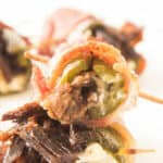 Close-up of Texas Twinkies: bacon-wrapped jalapeño poppers stuffed with cheese and meat, secured with toothpicks on a white background.