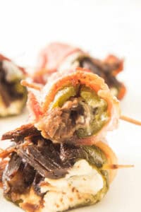 Close-up of Texas Twinkies: bacon-wrapped jalapeño poppers stuffed with cheese and meat, secured with toothpicks on a white background.