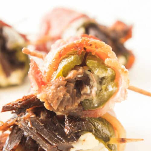 Close-up of Texas Twinkies: bacon-wrapped jalapeño poppers stuffed with cheese and meat, secured with toothpicks on a white background.