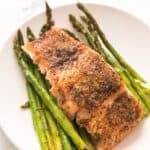A delicious piece of seasoned, cooked salmon is served atop roasted asparagus spears on a white plate, creating a classic Salmon and Asparagus pairing that’s both elegant and flavorful.