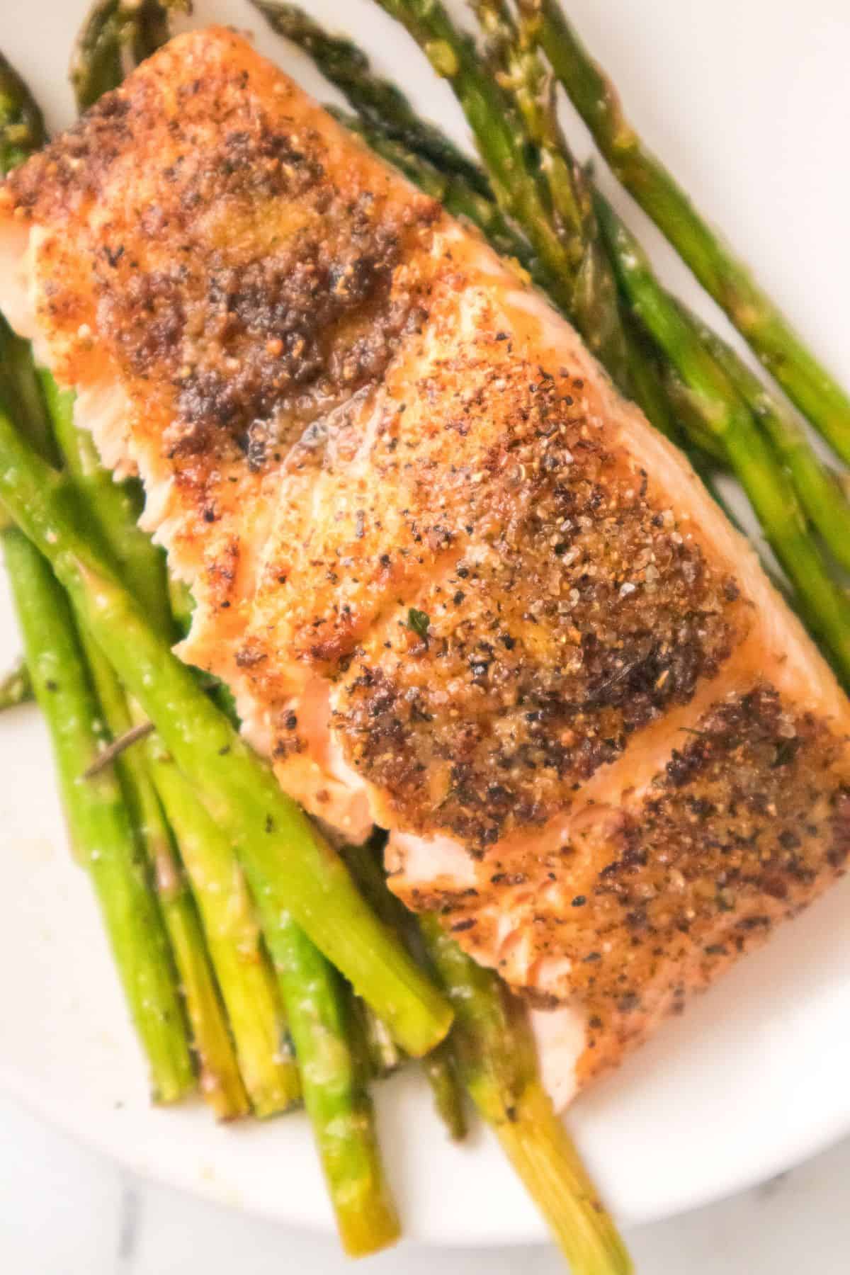 A seasoned, baked salmon fillet is elegantly served on a bed of roasted asparagus spears, showcasing the perfect harmony of salmon and asparagus on a pristine white plate.