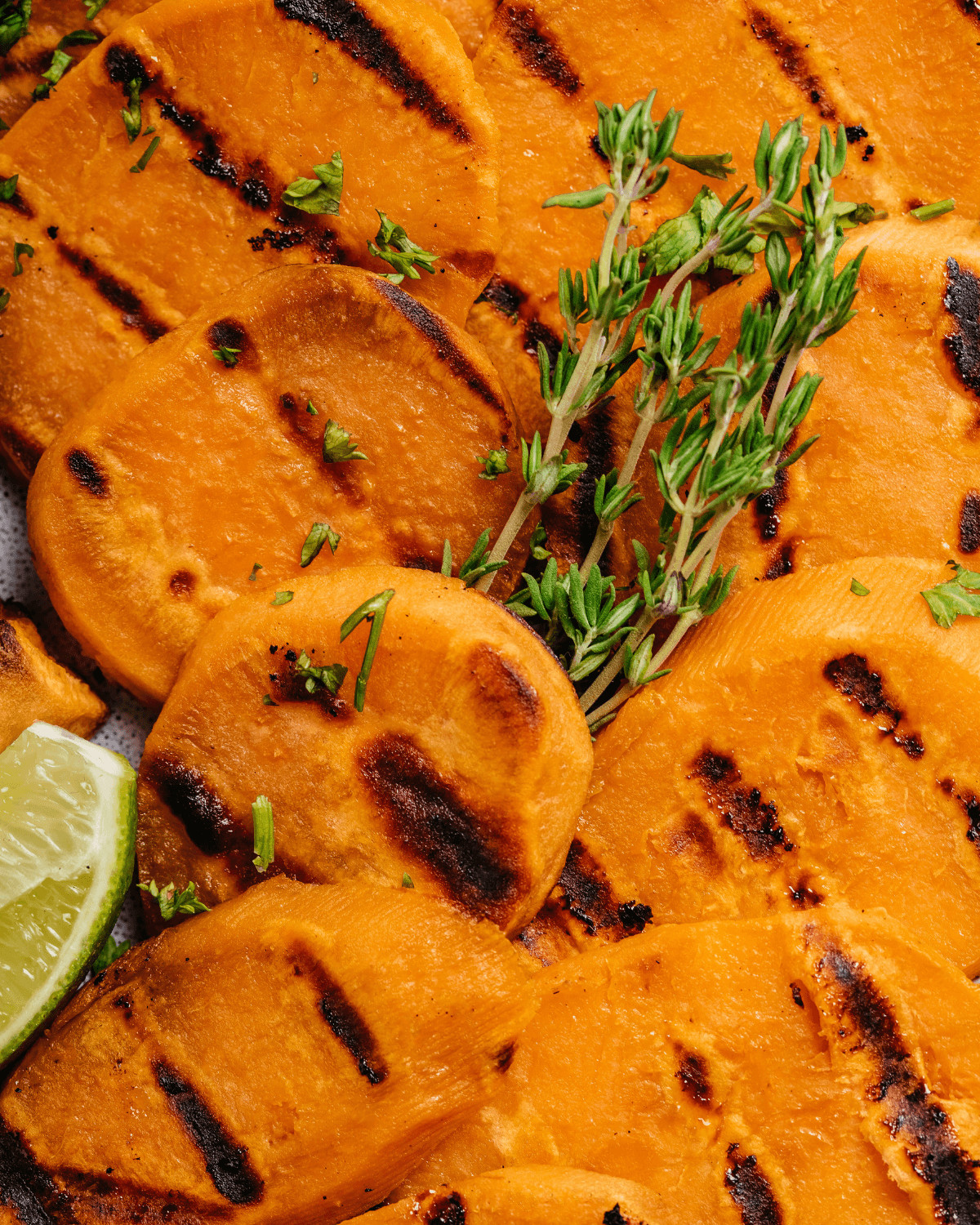 A closeup on the slices of sweet potatoes on the grill with grill marks.