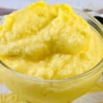 A clear glass bowl filled with thick, smooth, yellow Dole Pineapple Whip sits on a striped yellow and white cloth.