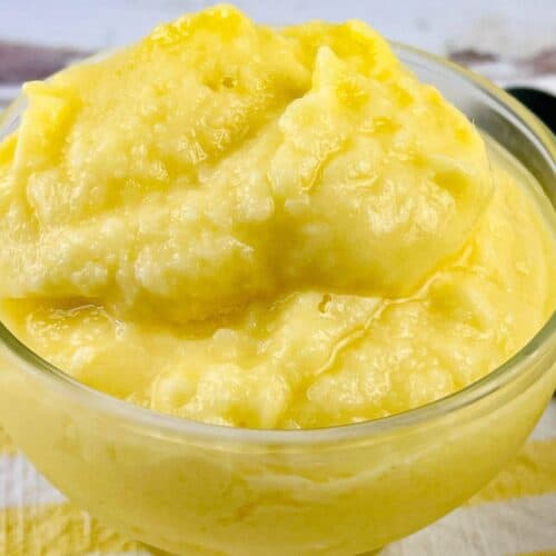 A clear glass bowl filled with thick, smooth, yellow Dole Pineapple Whip sits on a striped yellow and white cloth.