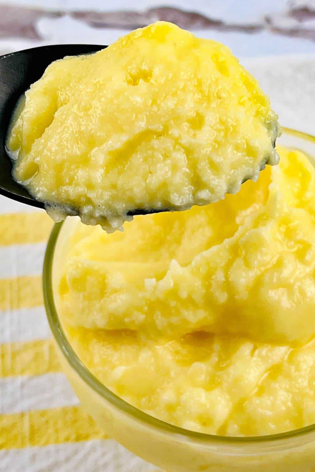 A close-up of a spoonful of yellow, creamy pudding taken from a bowl filled with the same dessert.