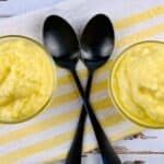 Two bowls of creamy yellow pudding, reminiscent of Dole Pineapple Whip, sit on a yellow and white striped cloth with two black spoons crossed in the center.